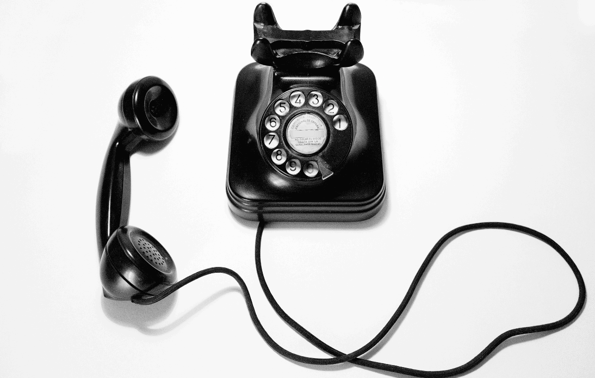 A rotary telephone with the receiver off the hook sits on a white background.