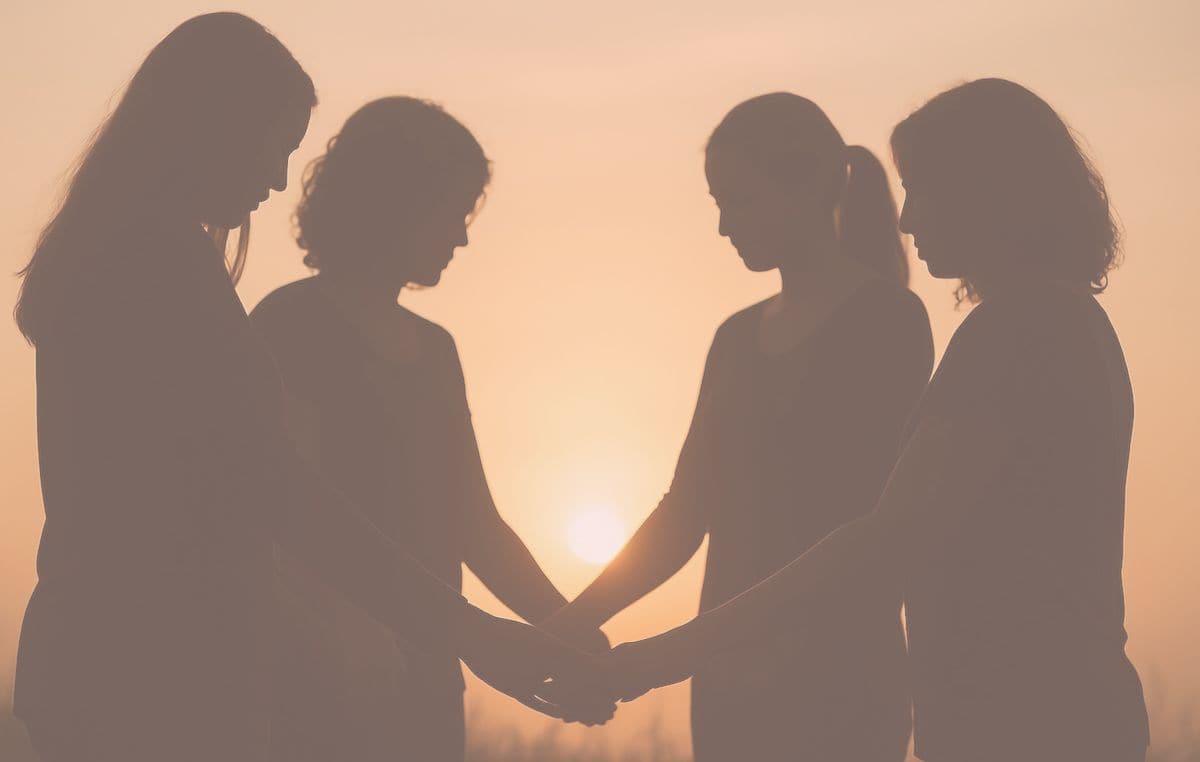 sisterhood-connection-widowhood Image showing silhouette of four women holding hands and praying together